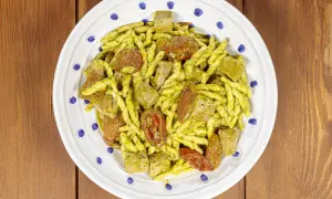 Piatto di trofie alla carlofortina con tonno, pomodorini secchi e pesto, servite su un piatto bianco con decorazioni blu.
