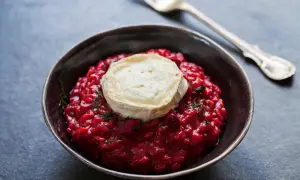Un cremoso risotto alla barbabietola, con una fetta di formaggio di capra fuso sopra e un rametto di erbe aromatiche.