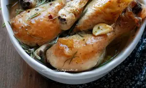 Cosce di pollo succulente, dorate e profumate al rosmarino e aglio, servite in una ciotola bianca.