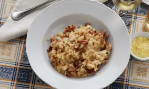 Un piatto di risotto alla pilota cremoso, con pezzetti di salsiccia, servito su una tovaglia a quadri.
