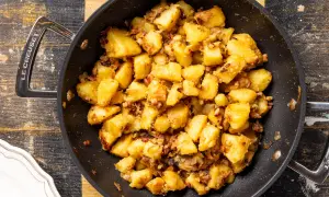 Patate in tecia dorate e croccanti, con pezzetti di pancetta e cipolla, pronte per essere gustate.