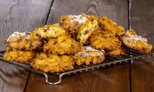 Biscotti croccanti, simili a rose del deserto, con uvetta e fiocchi di mais, spolverati di zucchero a velo su una griglia metallica.