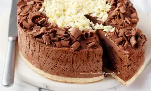 Delizioso semifreddo al cioccolato, ricoperto di riccioli di cioccolato fondente e bianco. Una fetta è stata tagliata, rivelando la sua consistenza cremosa.