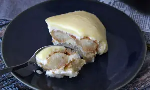 Una fetta di tiramisù al limone su un piatto blu, con un cucchiaino che ne preleva un assaggio.