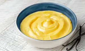 Una ciotola di cremosa crema pasticcera classica, con baccelli di vaniglia scuri accanto.