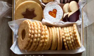Scatola piena di deliziosi dolci senza glutine: biscotti rotondi con stella al cioccolato, a forma di cuore con zucchero a velo, ricoperti di cioccolato e impilati in file ordinate.