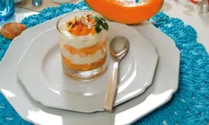 Delizioso semifreddo al melone a strati, guarnito con frutta fresca e mandorle, servito in un bicchiere su un piatto bianco.