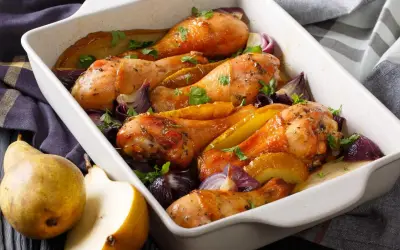 Cosce di pollo al forno croccante con pere e cipolle rosse in una teglia bianca.