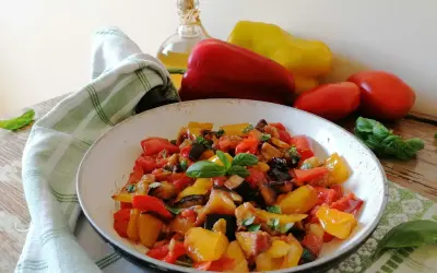 Un piatto colorato di peperonata con melanzane, pomodori e peperoni, guarnito con basilico fresco. La ricetta perfetta per un contorno estivo.
