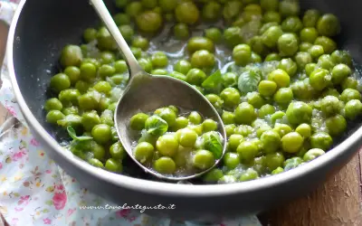 Piselli freschi in padella, cotti con cipolla e menta. Un cucchiaio ne raccoglie una porzione invitante.