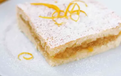 Una fetta di torta con pasta frolla morbida, ripiena di marmellata e spolverata di zucchero a velo e scorza d'arancia.