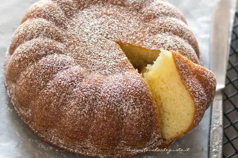 Una torta semplice e veloce, soffice e spolverata di zucchero a velo, con una fetta tagliata che ne mostra l'interno dorato.