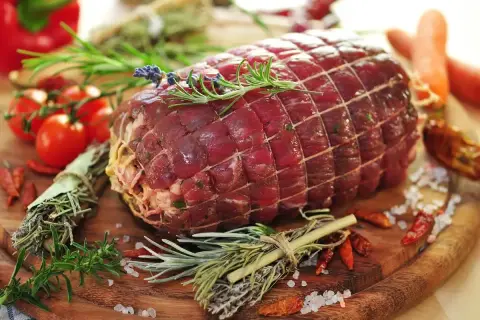 Un succulento arrosto di manzo, legato con spago e guarnito con rosmarino e lavanda, pronto per essere cucinato con pomodorini, peperoncini e carote.