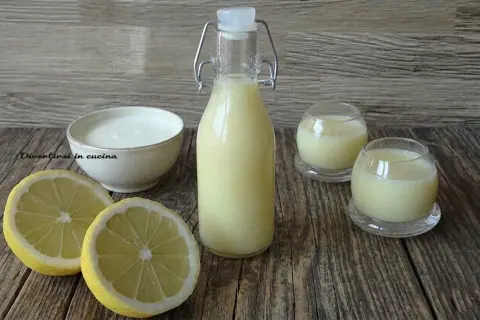 Una bottiglia e due bicchierini di crema di limoncello, con limoni freschi e una ciotola di panna.
