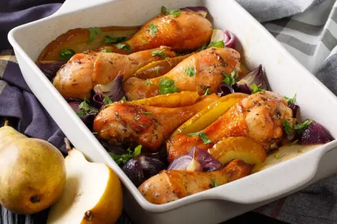 Cosce di pollo al forno croccante con pere e cipolle rosse in una teglia bianca.
