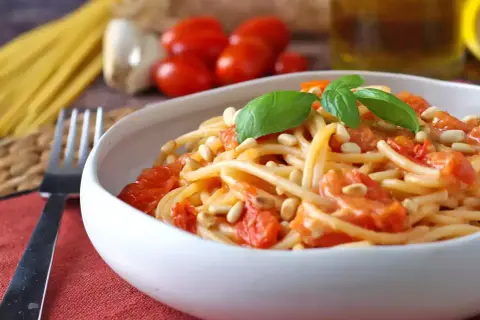 Un piatto invitante di spaghetti con pomodorini freschi, pinoli tostati e basilico, pronto per essere gustato.