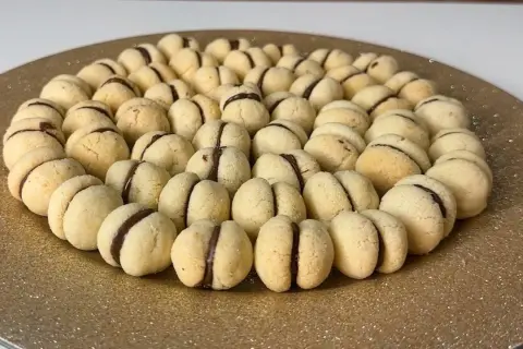 Un vassoio dorato pieno di deliziosi baci di dama, biscotti friabili con un cuore di cioccolato.