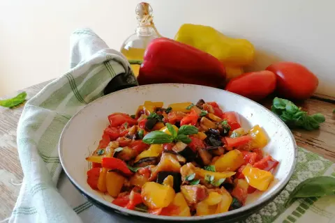 Un piatto colorato di peperonata con melanzane, pomodori e peperoni, guarnito con basilico fresco. La ricetta perfetta per un contorno estivo.