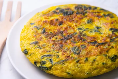 Frittata di spinaci dorata e soffice su un piatto bianco, con un utensile in legno sullo sfondo.