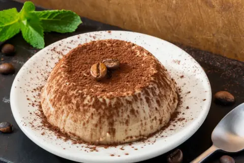 Deliziosa panna cotta al caffè, cosparsa di cacao e decorata con chicchi di caffè e menta fresca.