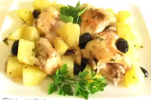 Coniglio in padella con patate e olive nere, guarnito con prezzemolo fresco. Un piatto saporito e invitante.