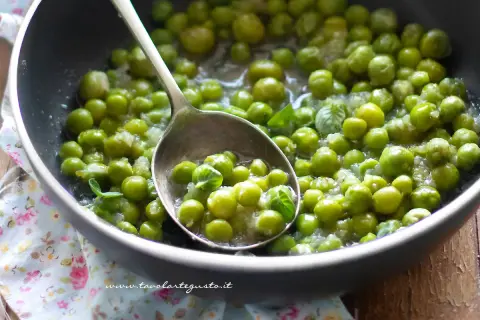 Piselli freschi in padella, cotti con cipolla e menta. Un cucchiaio ne raccoglie una porzione invitante.