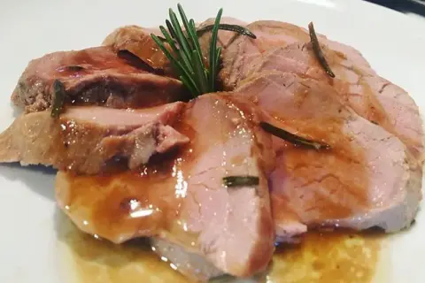 Fette succulente di filetto di maiale al forno, bagnate in un sughetto saporito e guarnite con rosmarino fresco.