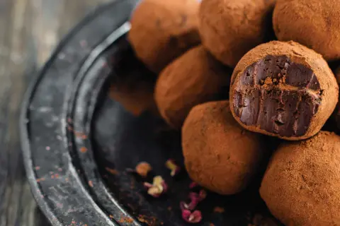 Un mucchio di tartufini al cioccolato ricoperti di cacao, uno aperto rivela il ripieno fondente.