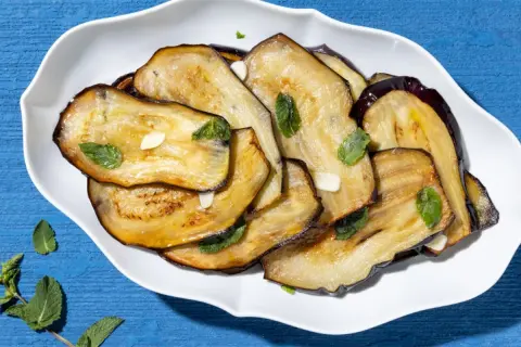 Fette di melanzane grigliate, condite con aglio e menta fresca, un contorno di verdure saporito e colorato.