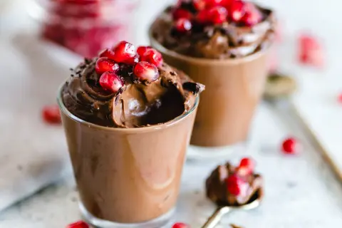 Due bicchierini di golosa mousse al cioccolato, guarniti con chicchi di melagrana e scaglie di cioccolato.