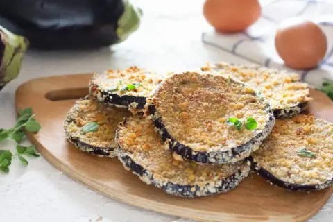 Fette di melanzane al forno impanate, dorate e croccanti, guarnite con erbe aromatiche fresche.