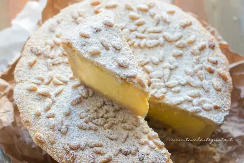 Torta della nonna facile, con crema gialla, pinoli e zucchero a velo. Una fetta è stata tagliata.