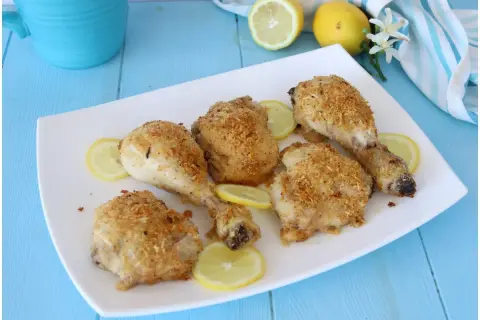 Cosce di pollo al limone croccanti e dorate, servite su un piatto bianco con fette di limone fresco.