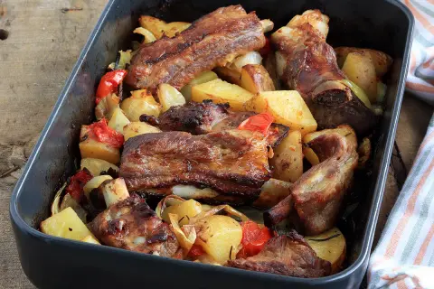 Puntine di maiale succulente al forno con patate, peperoni e cipolle in una teglia scura.