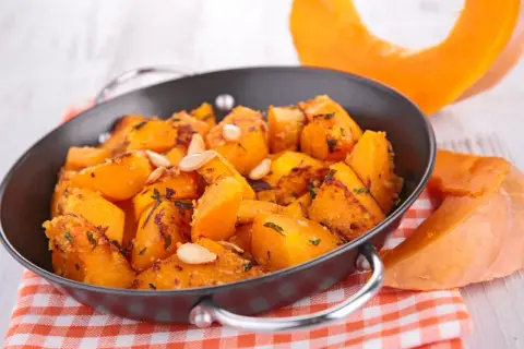 Zucca in agrodolce cotta in padella, guarnita con semi di zucca e erbe aromatiche. Un contorno autunnale saporito.