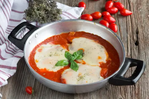 Un invitante pollo alla pizzaiola in padella, con mozzarella filante e basilico fresco, pronto per essere gustato.