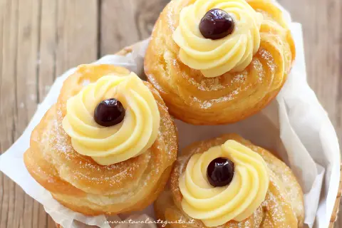 Tre zeppole di San Giuseppe, dolci fritti con crema pasticcera e ciliegina, spolverate di zucchero a velo.