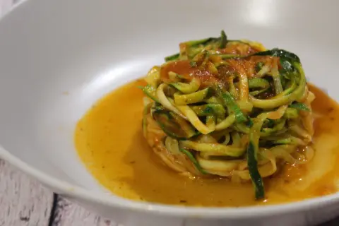 Un piatto di spaghetti di zucchine conditi con sugo rosso, serviti in una ciotola bianca.