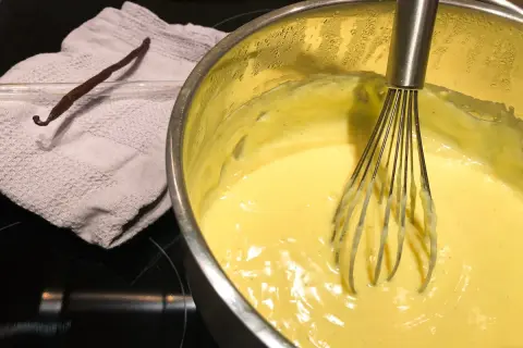 Crema pasticcera senza latte in preparazione, con bacca di vaniglia e frusta.