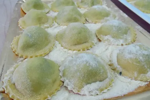 Un vassoio pieno di ravioli ricotta e spinaci freschi, spolverati di farina, pronti per essere cucinati.