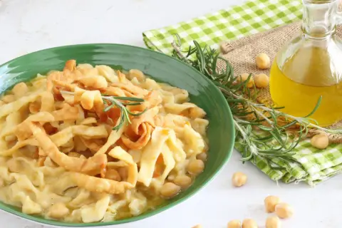 Piatto di ciceri e tria, pasta fresca con ceci, guarnito con rosmarino e croccanti straccetti fritti. Olio d'oliva e ceci sparsi intorno.