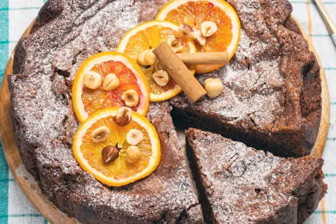 Torta di pane al cioccolato, decorata con fette d'arancia, nocciole e cannella, spolverata di zucchero a velo.