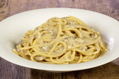 Un piatto di spaghetti cremosi al cacio e pepe, conditi con pepe nero macinato fresco.