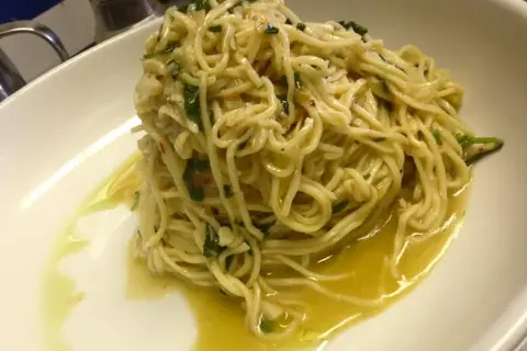 Un piatto di spaghetti aglio olio e peperoncino cremosi, conditi con prezzemolo fresco e un filo d'olio d'oliva, serviti in una ciotola bianca.