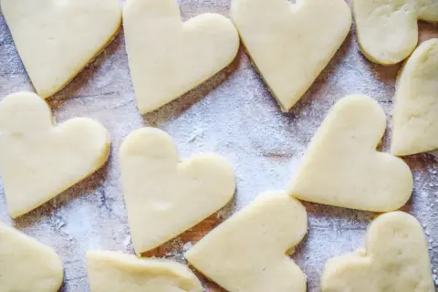 Cuore di biscotti senza burro spolverati di zucchero a velo su un tagliere di legno.