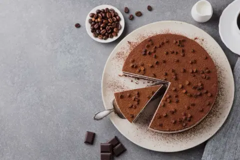 Una deliziosa torta al caffè, cosparsa di cacao e gocce di cioccolato, con una fetta servita. Chicchi di caffè e cioccolato completano la scena.