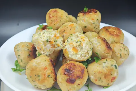 Un piatto di polpette di pollo dorate, con pezzetti di carota e prezzemolo visibili all'interno. Alcune sono leggermente aperte, mostrando la morbidezza.