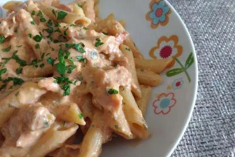 Penne al baffo cremose e saporite, condite con una salsa rosa e prezzemolo fresco, servite su un piatto decorato con fiori.