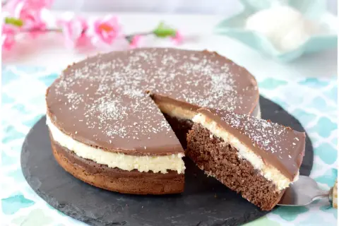 Deliziosa torta cocco e cioccolato, con una fetta appena tagliata, cosparsa di cocco grattugiato.