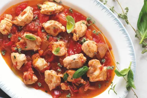 Piatto di coniglio alla cacciatora ricetta della nonna, con pezzi di carne tenera in salsa di pomodoro e peperoni, guarnito con basilico fresco e timo.